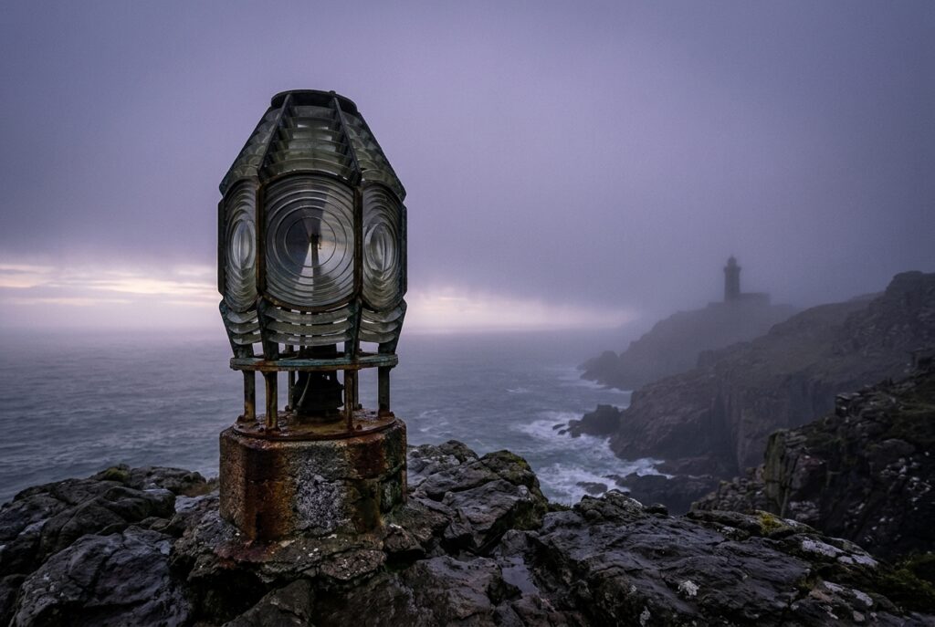 Lanterne de phare posée sur un rocher face à une mer brumeuse